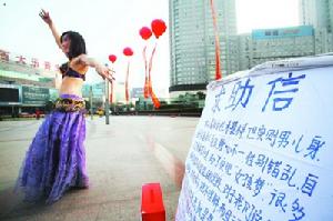 11月26日下午,在市府廣場,一位“舞娘”在人群中跳起了肚皮舞。然而,如果不看“她”寫在木板上的求助信,誰也難以看出,眼前這位舞姿翩翩的嬌媚舞娘,其實是男兒身。