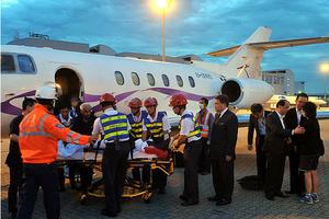 載著梁頌學的醫療專機晚上抵達香港機場,早已在場等候的醫管局主席胡定旭(右五)及救護人員小心翼翼地將他送上救護車,直奔屯門醫院接受治療